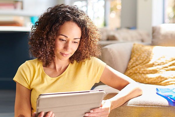 Woman wearing yellow looking at a tablet sitting in front of her couch on the floor