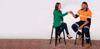 Two people sitting on stools sharing a fist bump